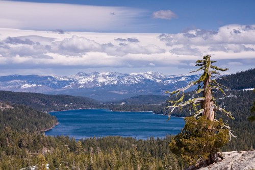 A scenic view of a lake surrounded by mountains and forests under a partly cloudy sky.