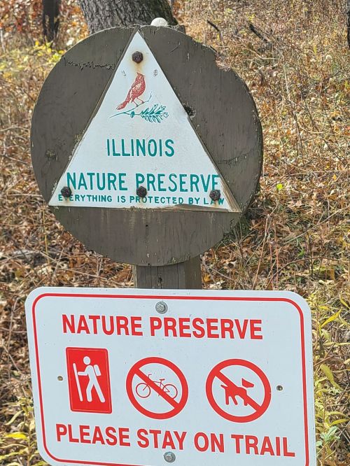 Sign for an Illinois nature preserve, featuring a bird illustration and warnings to stay on the trail.