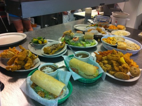 A variety of dishes on a table, including sandwiches, fried chicken, salads, and sides in a casual dining setting.
