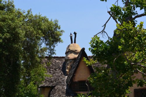 A whimsical building with a unique, rounded roof and two tall, pointed structures, surrounded by trees and blue sky.