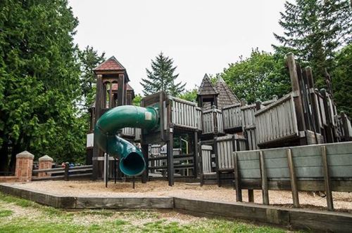 A playground featuring a green slide, wooden structures, and surrounding trees on a cloudy day.