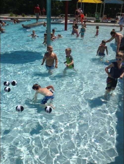Children playing in a shallow pool, splashing water and enjoying the sun, with beach balls scattered around.