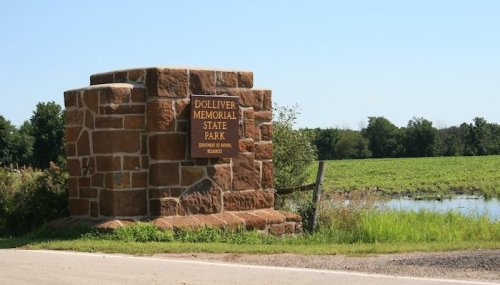 Stone entrance sign for Dolliver Memorial State Park, surrounded by greenery and a pond in the background.