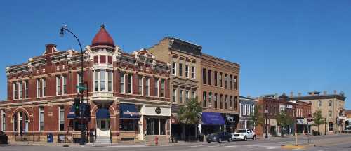 Historic buildings line a sunny street, showcasing brick architecture and a clear blue sky.