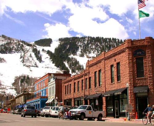 A historic street lined with colorful buildings, set against a snowy mountain backdrop under a blue sky.