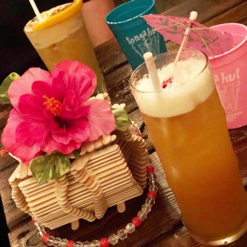 A vibrant tropical drink with a flower garnish, surrounded by colorful cups and a decorative floral centerpiece.