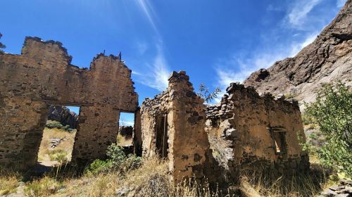 Ruins of an old stone building surrounded by tall grass and rocky terrain under a clear blue sky.