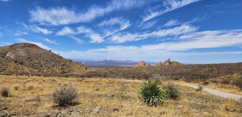 A scenic landscape featuring rolling hills, rocky formations, and a clear blue sky with wispy clouds.