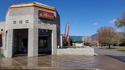 Exterior of El Agaveño, a Mexican restaurant, featuring a sign and a flag, with a clear blue sky in the background.