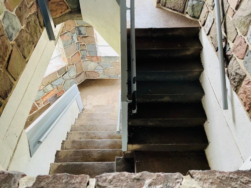 A view of a staircase with stone walls, leading down from a landing to a lower level.