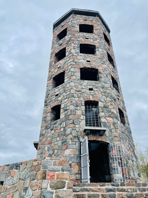 A tall stone tower with multiple windows and a barred entrance, set against a cloudy sky.