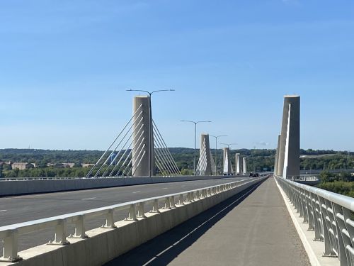 A modern cable-stayed bridge with tall pillars and cables, set against a clear blue sky and green landscape.