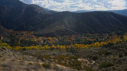 A scenic view of mountains with autumn foliage in a valley, under a partly cloudy sky.