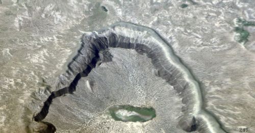 Aerial view of a large, circular crater with a central lake surrounded by rugged terrain and dry landscape.