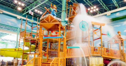 A colorful indoor water play structure with slides, water features, and a large character figure on top.