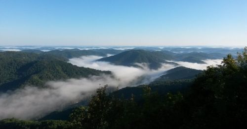 A panoramic view of misty mountains under a clear blue sky, with fog rolling through the valleys.