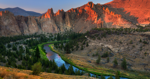 A scenic view of a river winding through a canyon, surrounded by rocky cliffs and lush greenery at sunset.