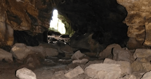 A dark cave entrance with scattered rocks and a bright light shining through the opening in the background.