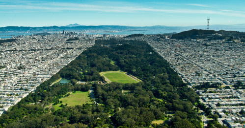 Aerial view of a city with a large park in the center, surrounded by urban development and distant hills.