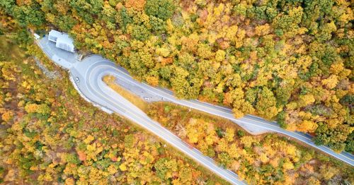 Aerial view of winding roads surrounded by vibrant autumn foliage in a mountainous area.