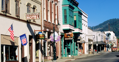 Historic street scene featuring colorful storefronts and American flags in a small town. Mountains in the background.