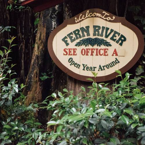 Sign reading "Welcome to Fern River, See Office A, Open Year Around," surrounded by greenery and trees.