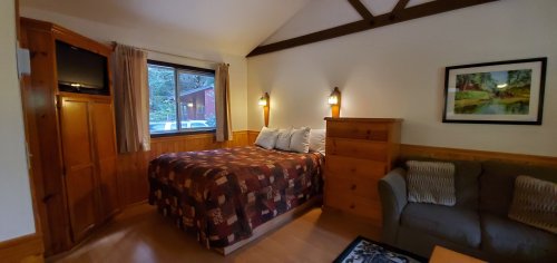 Cozy bedroom with a queen bed, wooden furniture, a sofa, and a window overlooking a natural setting.