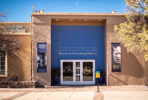 Entrance of the Museum of International Folk Art, featuring banners and a blue wall with text about craftsmanship.