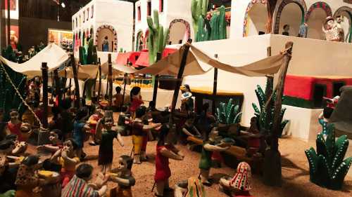 Colorful scene of a festive market with miniature figures, tents, and cacti, depicting a lively celebration.