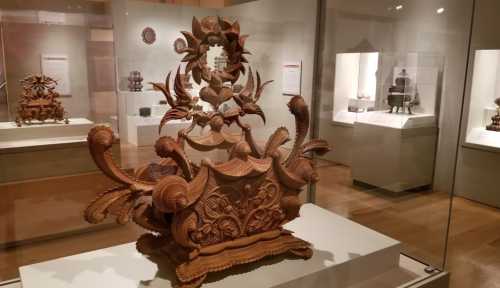 Intricate wooden sculpture with ornate carvings displayed in a museum, surrounded by other art pieces.