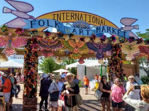 Colorful entrance archway to the International Folk Art Market, bustling with visitors and vibrant decorations.