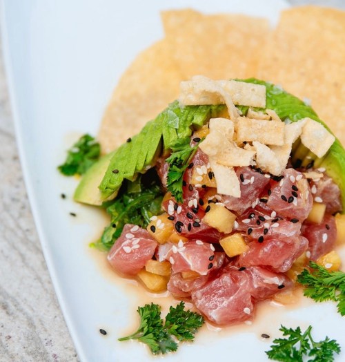 A vibrant dish featuring diced tuna, avocado, and crispy toppings, garnished with herbs and served with tortilla chips.