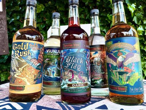 Five bottles of rum with colorful labels, featuring designs like skulls and tropical themes, set against a green backdrop.