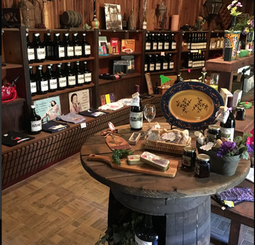 A cozy shop interior featuring shelves of bottles, a wooden table with snacks, and decorative items.