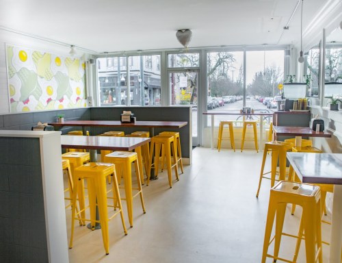 Bright, modern café interior with yellow stools, large windows, and colorful wall art featuring eggs and ice cream.