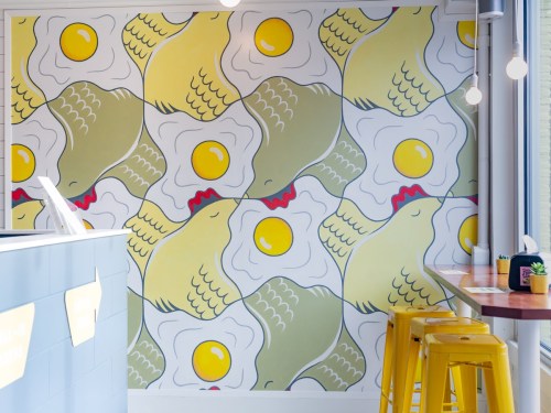 Colorful mural featuring chickens and eggs, with a modern dining area and yellow stools in the foreground.