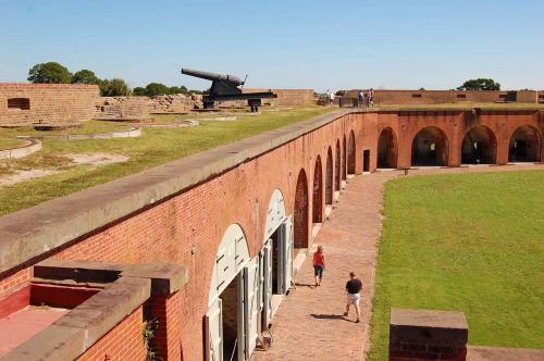 A historic fort with brick arches, grassy areas, and a large cannon on display under a clear blue sky.