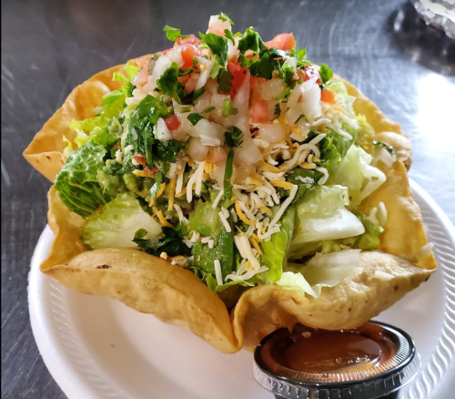A crispy tortilla bowl filled with lettuce, cheese, diced tomatoes, cilantro, and a side of salsa.