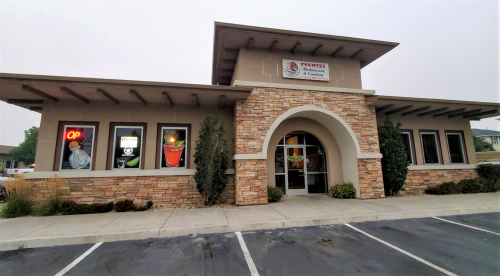 Exterior of a restaurant with stone accents, large windows, and a welcoming entrance, surrounded by greenery.