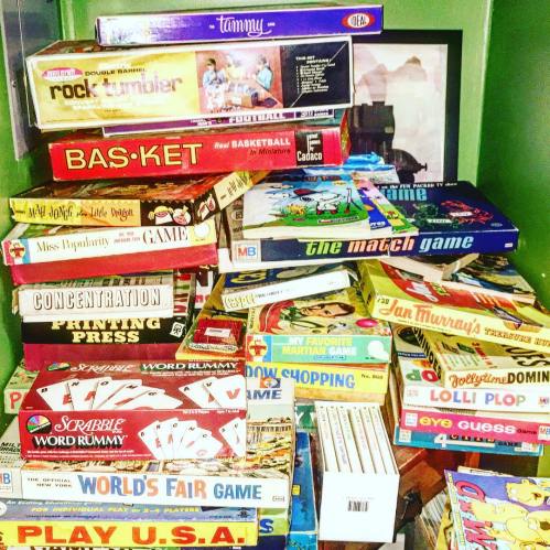 A colorful collection of board games stacked on a shelf, including Scrabble, Concentration, and various classic games.