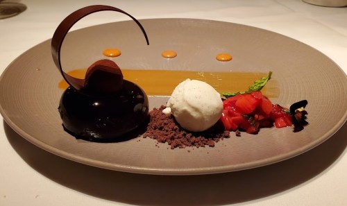 A gourmet dessert featuring chocolate mousse, vanilla ice cream, strawberry garnish, and a caramel sauce drizzle.