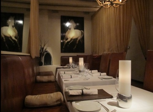 Elegant restaurant interior with a long table set for dining, featuring horse paintings and soft lighting.