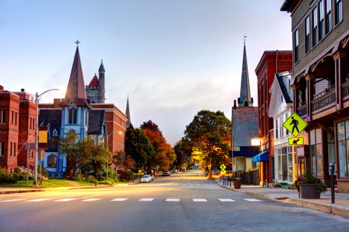 A quiet street scene at dusk, featuring historic buildings, church spires, and autumn foliage.