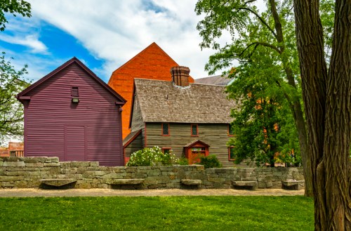 Historic buildings with varied architecture surrounded by greenery and stone walls under a partly cloudy sky.