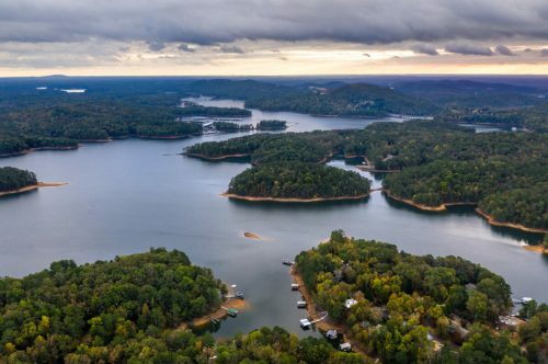 Aerial view of a serene lake surrounded by lush green islands and rolling hills under a cloudy sky.