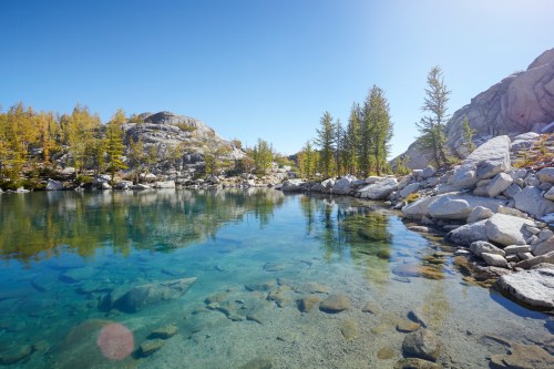 A serene lake surrounded by rocky terrain and golden trees under a clear blue sky.