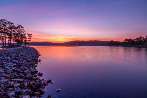 A serene lake at sunset, with vibrant colors reflecting on the water and trees lining the shore.
