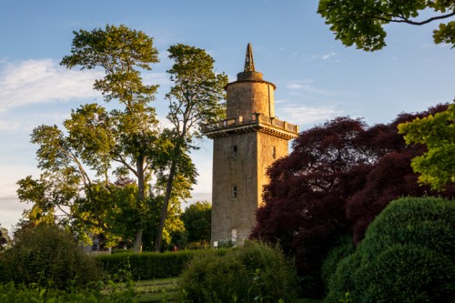 A historic tower surrounded by lush trees and greenery under a clear blue sky.