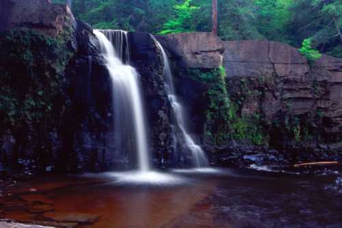 A serene waterfall cascading over rocky cliffs into a calm pool, surrounded by lush green foliage.