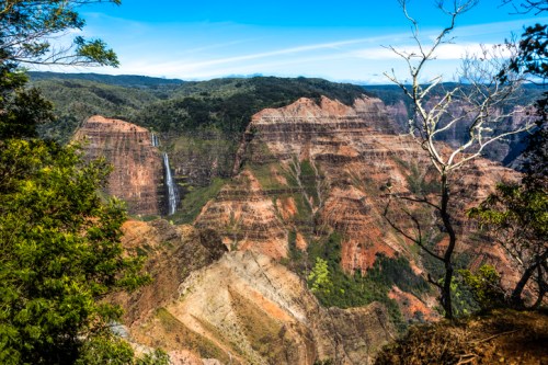 A stunning view of a canyon with layered red rock formations and a waterfall cascading down the cliffs.